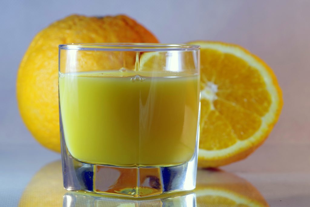 a small glass of orange juice with oranges in the background