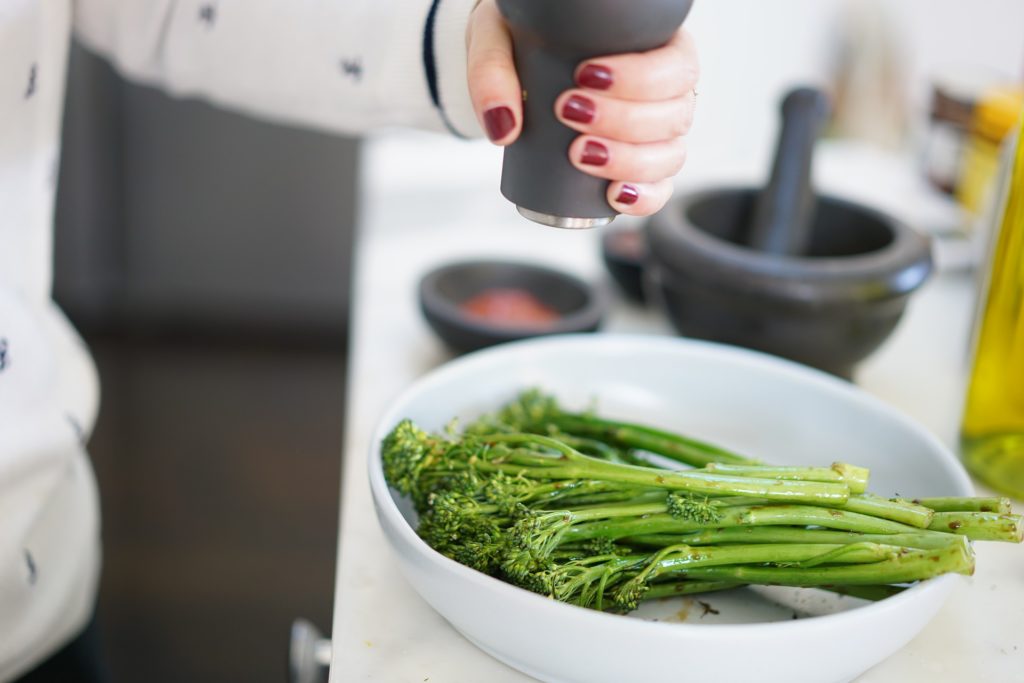 a woman's hand seasoning broccolini in a dish
