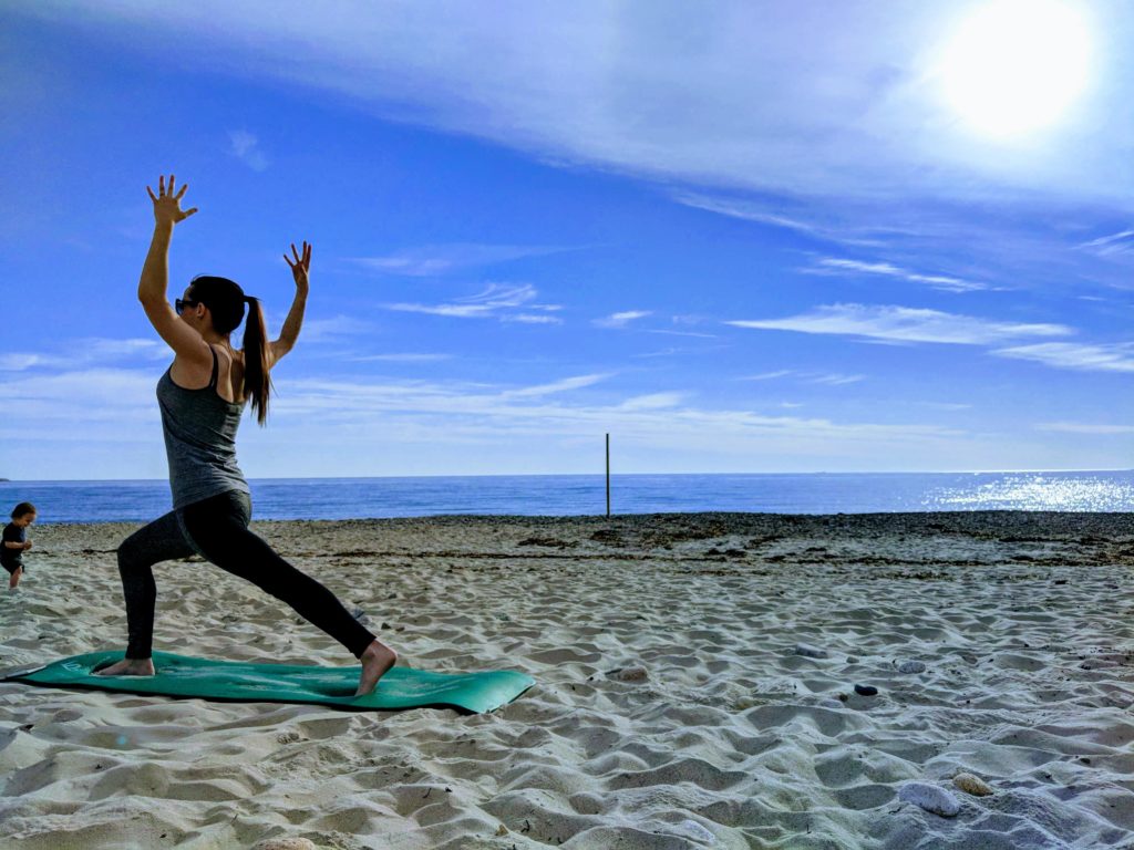 woman doing yoga on beach, toddler nearby